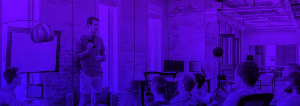 Palestrante se apresentando em um ambiente moderno e criativo, com participantes atentos em uma sala iluminada e decorada.