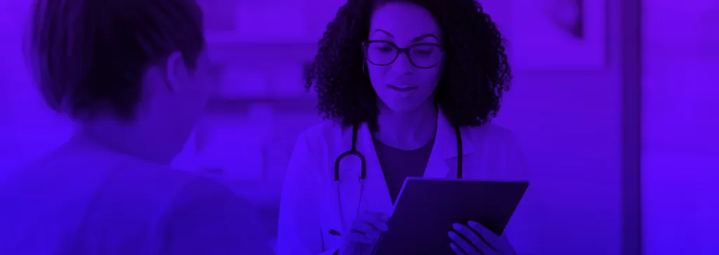 Médica utilizando um tablet em consulta, com um paciente do lado, ambiente de saúde moderno e tecnologia aplicada no atendimento médico.